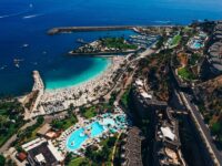 Aerial view of tropical Gran Canaria resort with beach, pools, marina, and vibrant atmosphere.