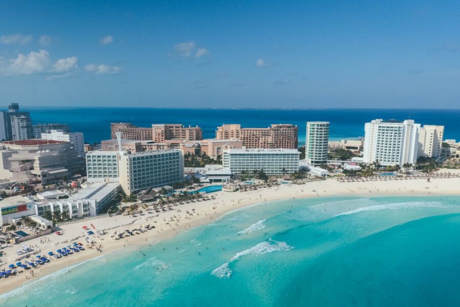 Aerial view of Cancun beach, turquoise waves, vibrant resorts, and beachgoers under sunny skies.