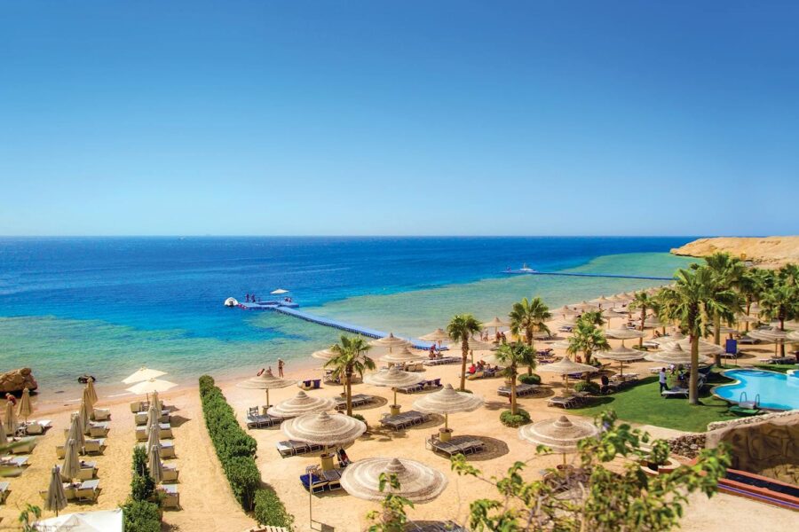 Luxury Red Sea beach resort with sun loungers, pier, palm trees, and oceanfront swimming pool.