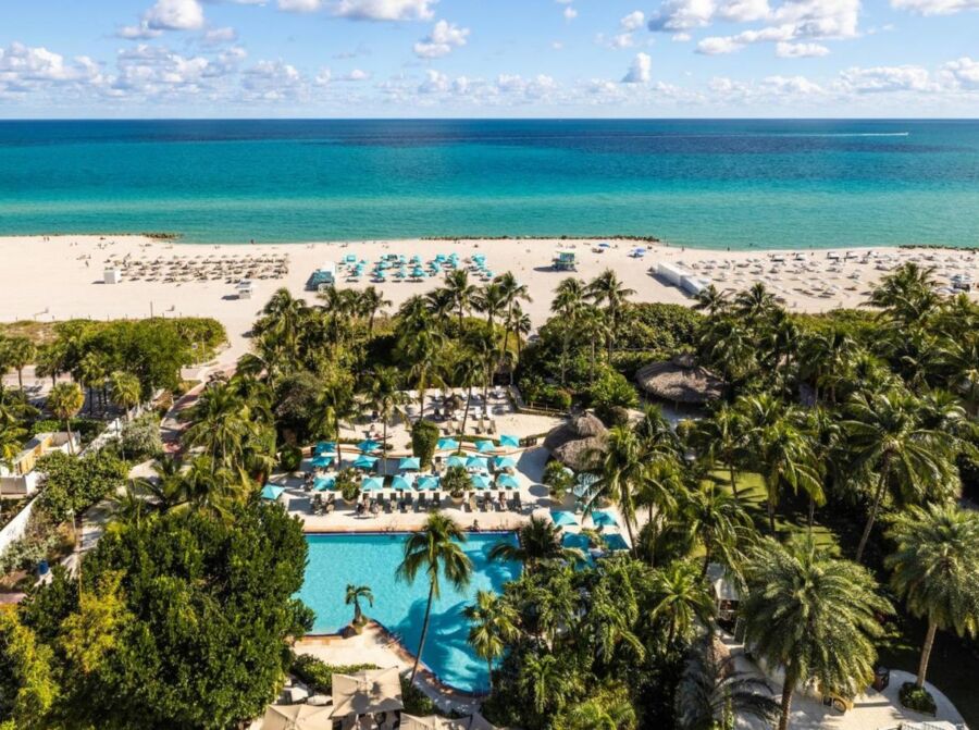 Luxury tropical resort with turquoise waters, palm trees, sandy beach, and inviting pool.
