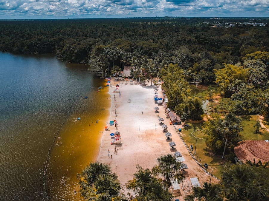 Aerial view of beach with sunbathers, colorful umbrellas, boats, and lush greenery.
