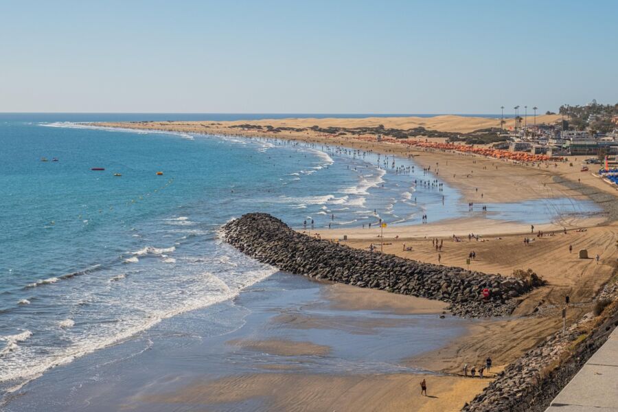 Idyllic beach with clear water, golden sands, and beachgoers enjoying leisure activities.