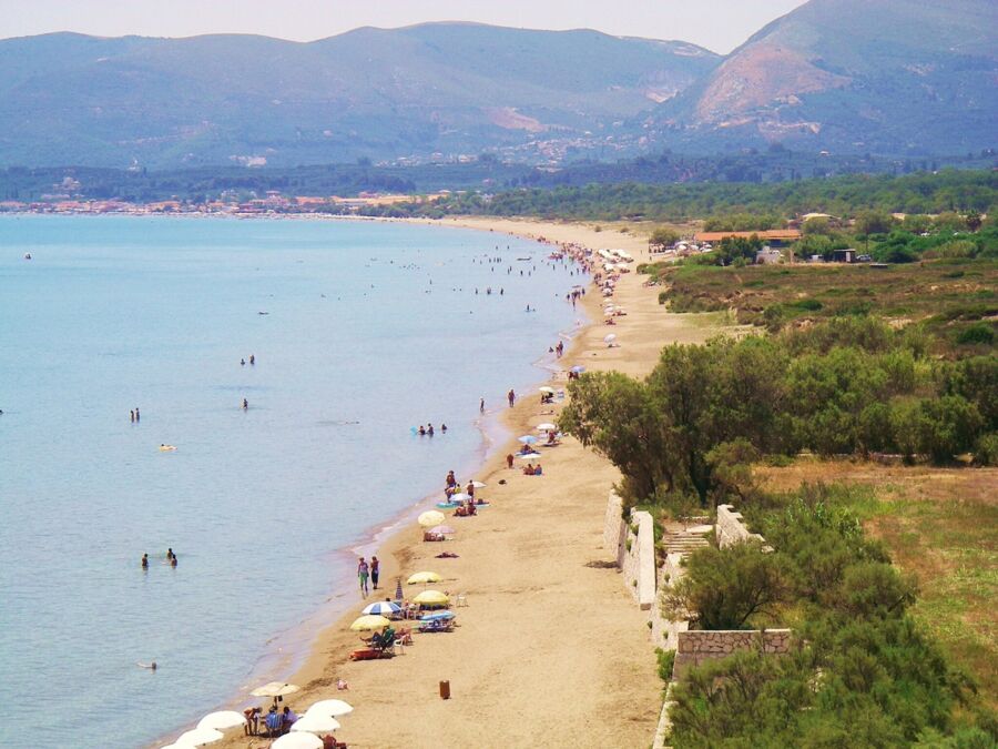 Colorful umbrellas dot a serene beach with turquoise water, sunbathers, and scenic hills.