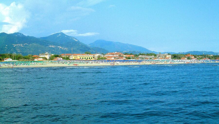 Picturesque Forte dei Marmi beach scene with turquoise sea, golden sand, lush hills, and colorful umbrellas.