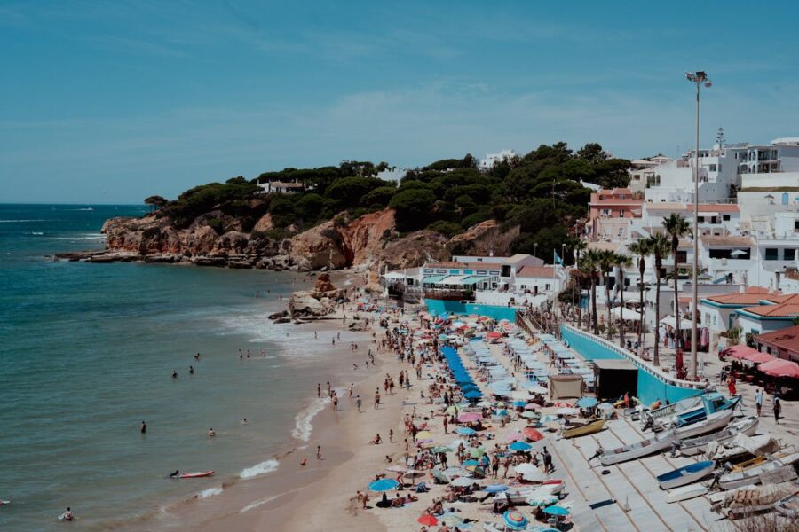 Sunny Albufeira beach with colorful umbrellas, rocky cliffs, and people enjoying summer activities.