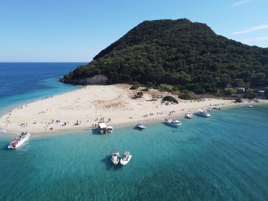 Idyllic coastal beach scene with turquoise waters, lush greenery, boats, and sunbathers.