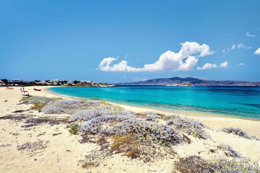 Idyllic beach scene with kayaks, turquoise water, sandy shore, and clear sky.