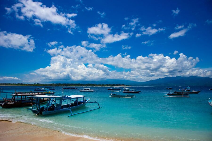 Turquoise coast with traditional boats, sandy shore, blue sky, mountains, evoking serenity.