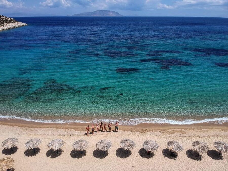 Turquoise ocean, sandy beach, island in the distance, people enjoying a sunny day.