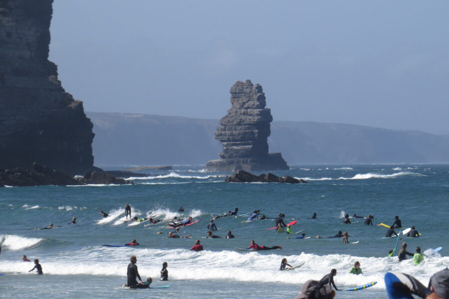 Surfers at Arrifana beach, Portugal, with sea stack and cliffs in Atlantic waves.
