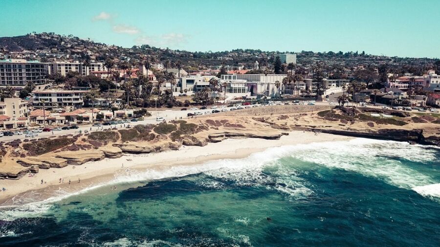 Vibrant La Jolla beach scene with ocean, palm trees, and coastal architecture.