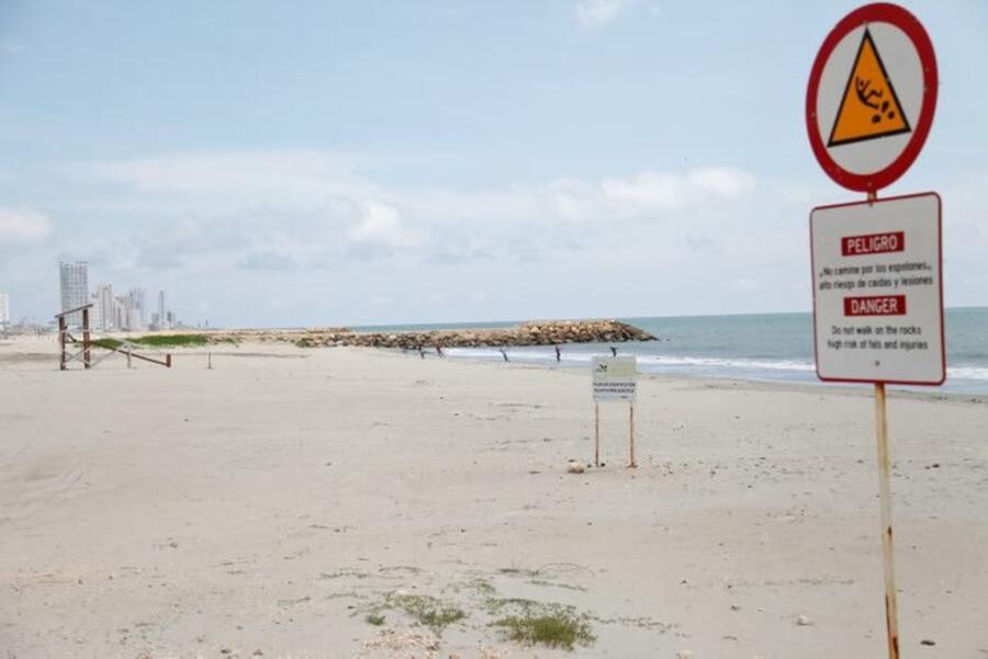 Tranquil beach scene with safety warning signs near urban resort and rocky shore.