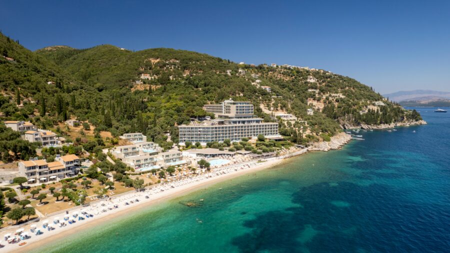 Aerial view of a coastal resort with beach, sea, and lush green hills.