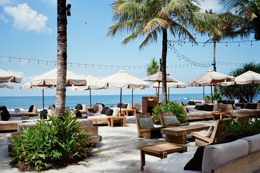 Luxury beachfront lounge with palm trees, ocean view, sunbeds and umbrellas at tropical beach resort.