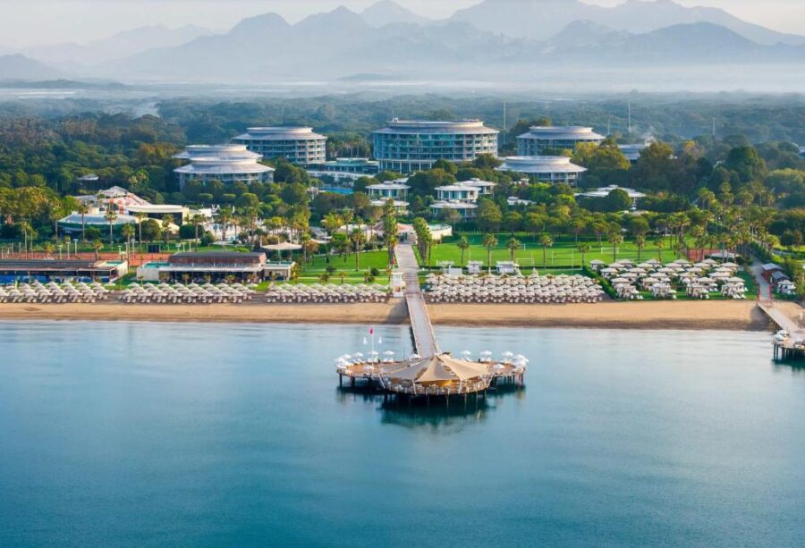 Luxury beachfront resort with pier, cabanas, pools and mountain backdrop on the Turkish Riviera.