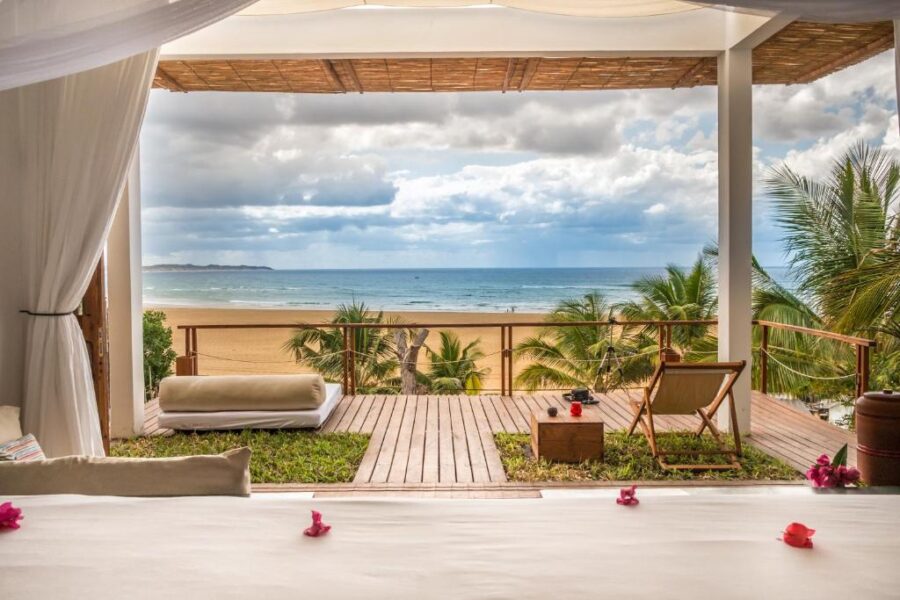 Luxury beachfront bedroom with oceanview terrace, canopy bed, tropical palm trees, and serene sandy beach.