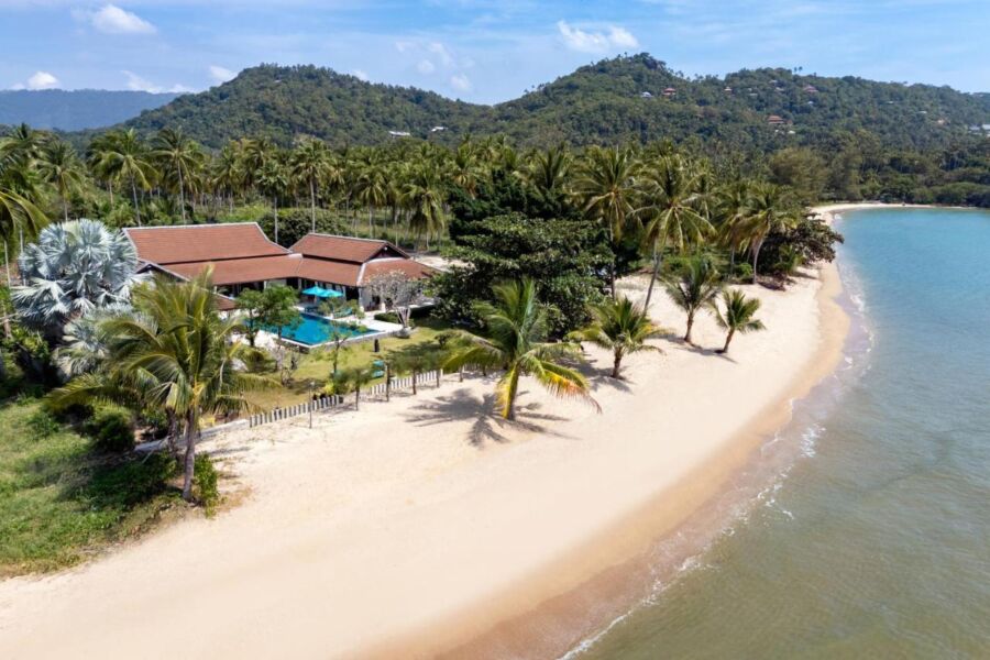 Serene beachfront property with tropical greenery, sandy beach, and azure sea in idyllic setting.