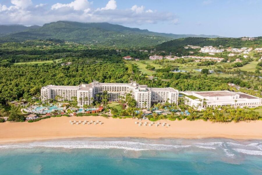 Aerial view of luxury beachfront resort in Puerto Rico with sandy beach, cabanas, mountains and ocean.