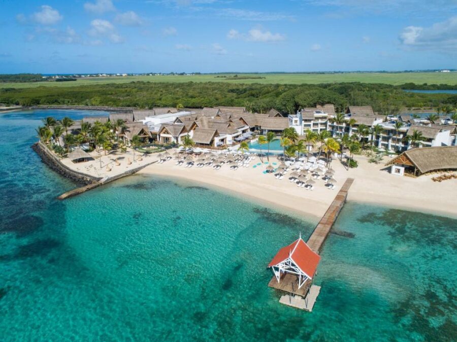 Aerial view of luxury Mauritius beachfront resort with infinity pool, pier, palm trees and turquoise lagoon.