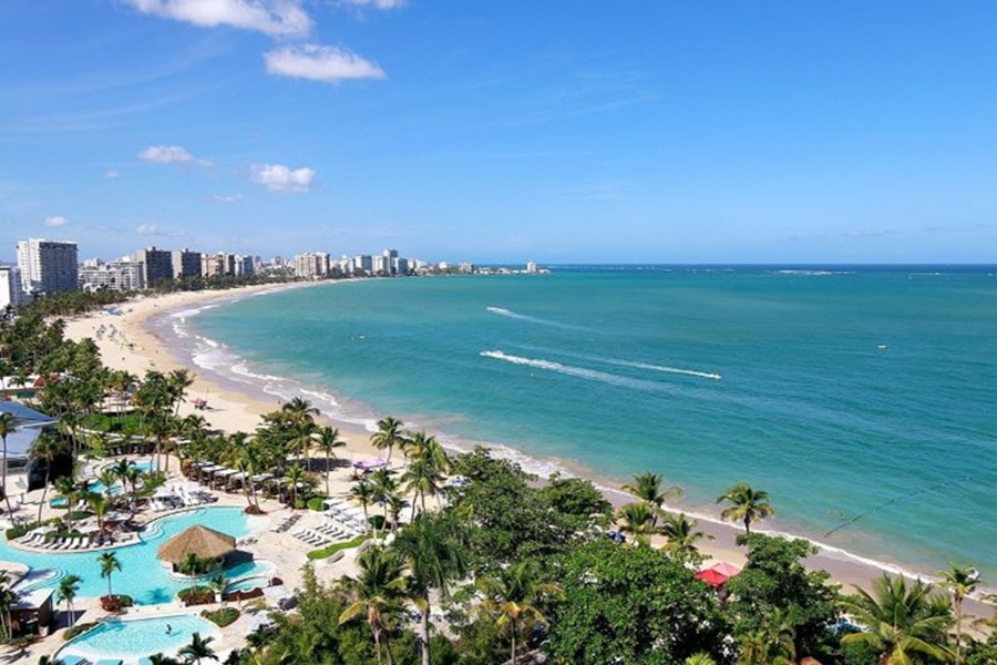 Tropical beachfront resort with pools, palm trees, luxury hotels, and turquoise ocean in Isla Verde.