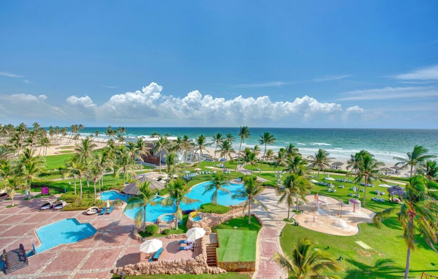 Luxury beachfront resort with tropical pool, palm trees, white sand beach, and ocean view.