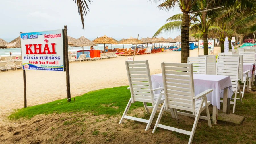 Beachfront Vietnamese seafood restaurant with oceanfront dining, palm trees, lounge chairs, and thatched umbrellas.