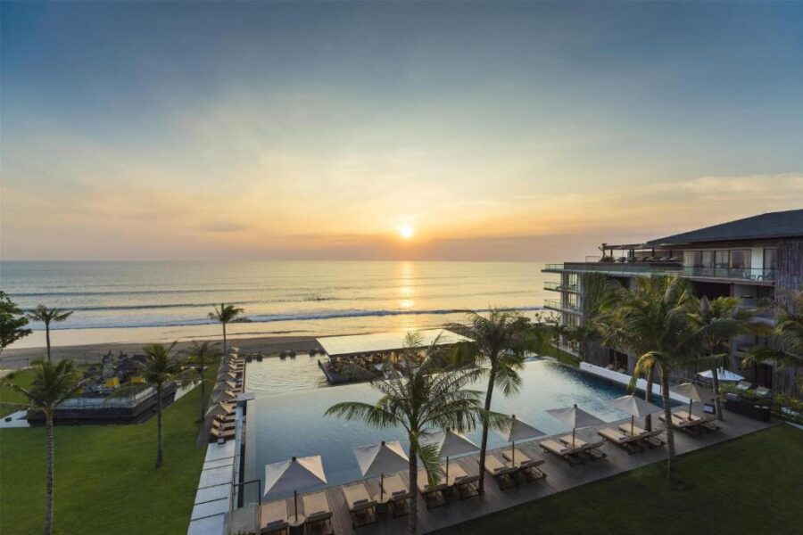 Luxury beachfront resort infinity pool at sunset with ocean view, palm trees, and modern hotel.