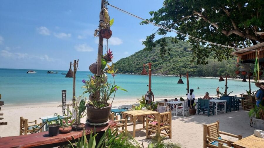 Tropical beach with turquoise waters, rustic beachfront restaurant, and lush green hills.