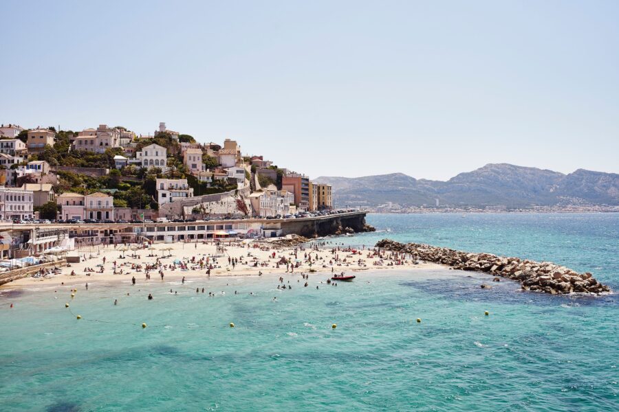 Vibrant Mediterranean beach scene with turquoise waters, lively activities, and scenic hillside architecture.