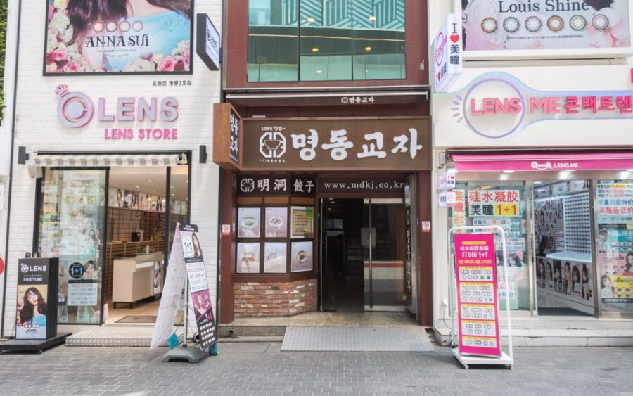 Urban shopping scene with lens stores and Myeongdong Gyoja restaurant.
