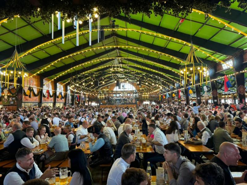 Crowded beer hall festival with long communal tables and people raising steins.