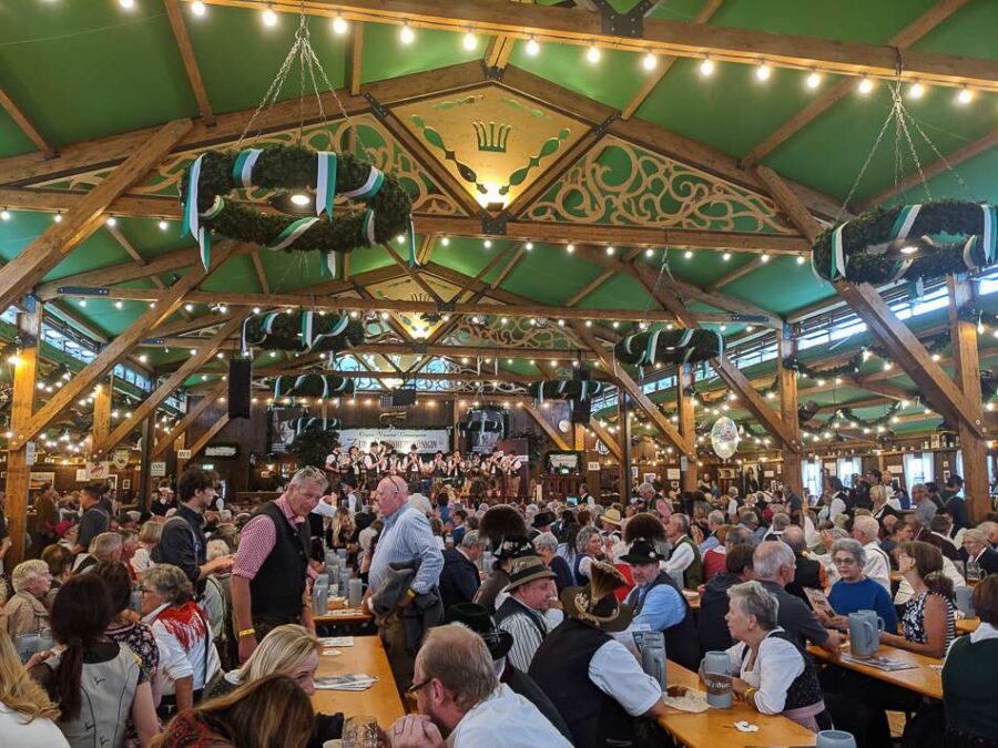 Beer hall festival with wooden beams, long tables, and crowd in Bavarian attire.