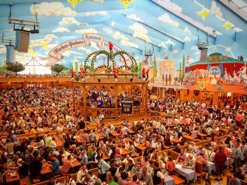 Oktoberfest crowded beer tent with Bavarian bandstand, tables, and beer steins.