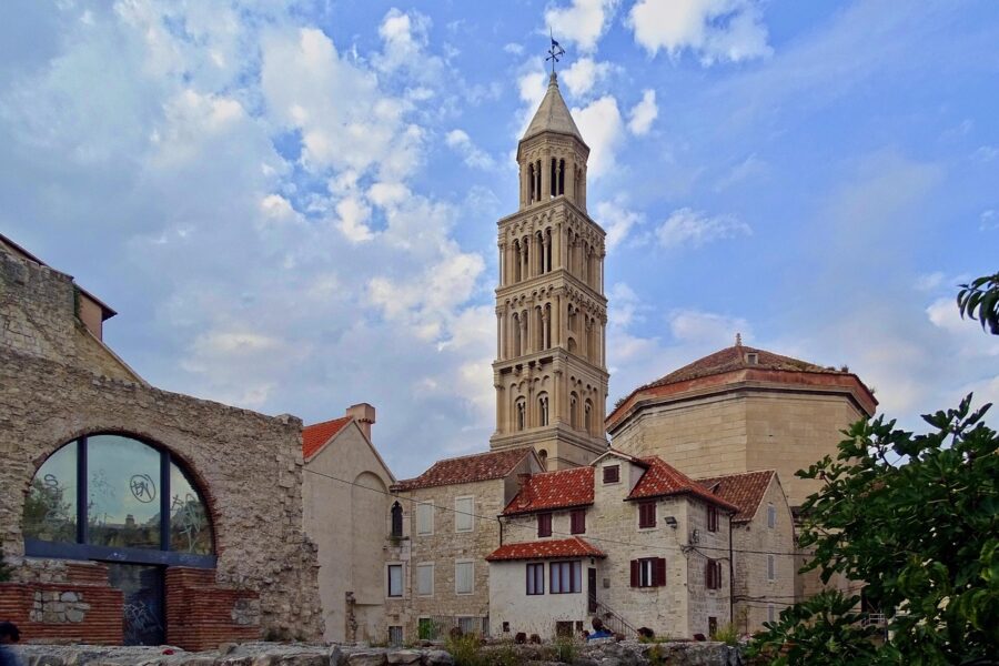 Historic bell tower with dome and stone architecture amid blue sky and greenery.