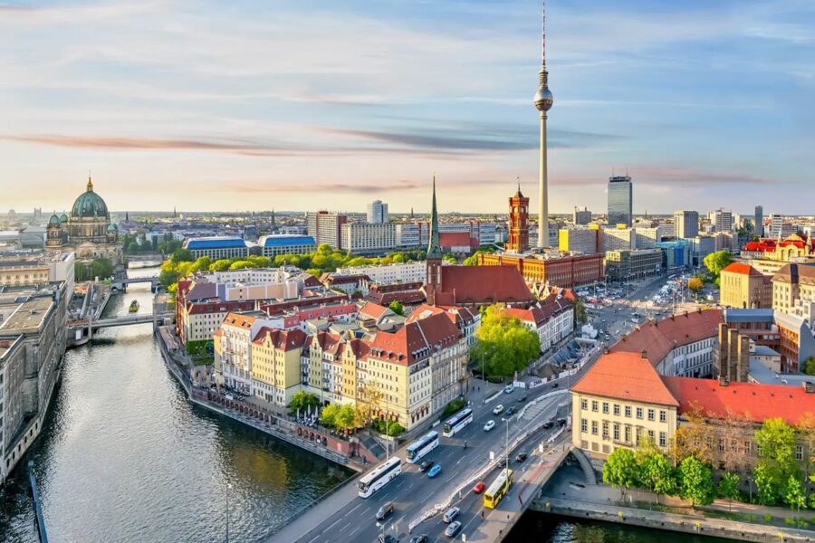 Aerial view of Berlin, showcasing historical and modern architecture by the river at sunset.