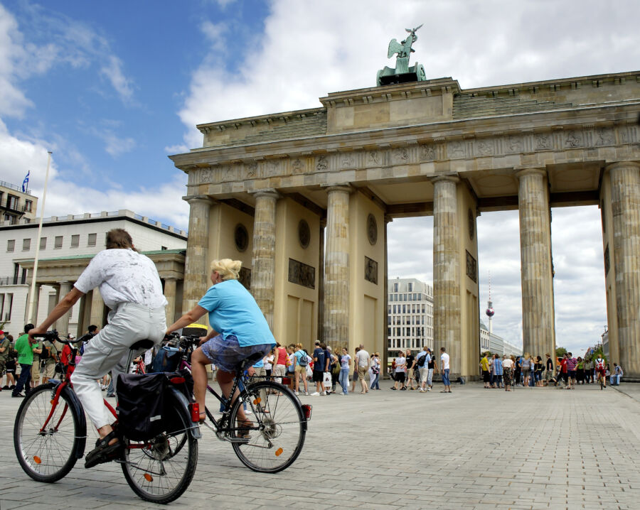 Couple enjoys a bike ride in front of the iconic Brandenburg Gate in Berlin, surrounded by historic architecture