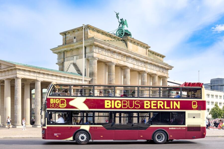 Berlin double-decker sightseeing bus in front of Brandenburg Gate with tourists.