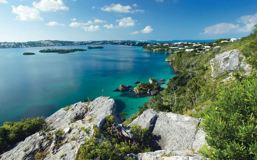 Breathtaking Bermuda coastline with turquoise waters, rocky shores, lush greenery, and distant islands.