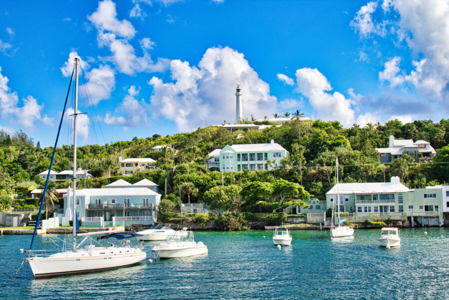 Boats docked in a sunny Bermuda harbor, with clear blue skies and calm waters reflecting the vibrant coastal town.
