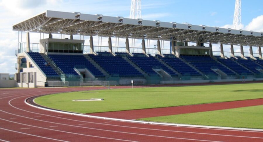 Exterior view of Bermuda National Sports Centre, showcasing its athletic fields and modern architecture against a blue sky.