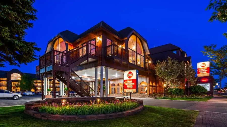 Best Western Plus Mackinaw City hotel exterior at dusk with lights, parking lot, and landscaped entrance.
