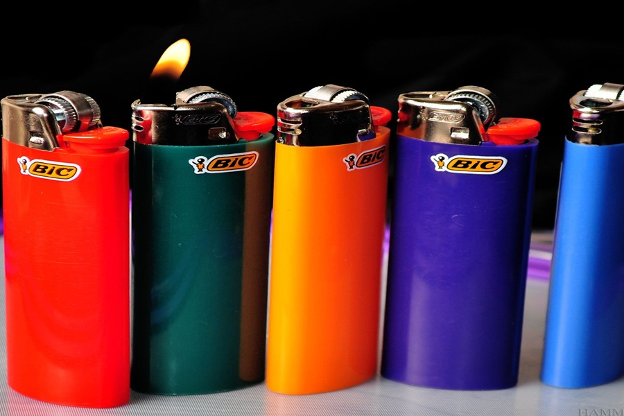 Colorful BIC lighters lineup with ignited flame, showcasing vibrant design against a dark background.