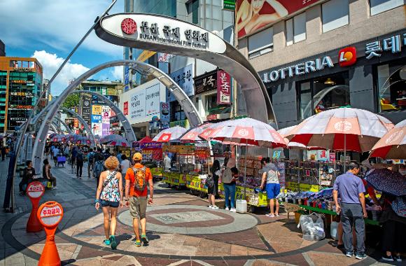 Korean street market festival with tourists, food stalls, umbrellas and BUAN Mudflat International Film Festival arch.
