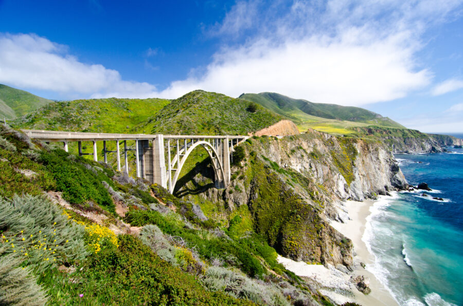 Bixby Bridge spanning a canyon on California's Highway 1, surrounded by rugged cliffs and coastal scenery in Big Sur.
