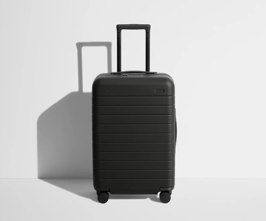 Black Bigger Away Carry-On suitcase with wheels resting on a white surface.
