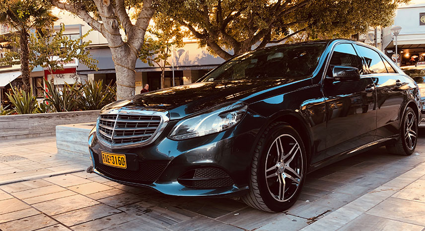 Black Mercedes-Benz luxury sedan parked on tiled urban plaza at golden hour.