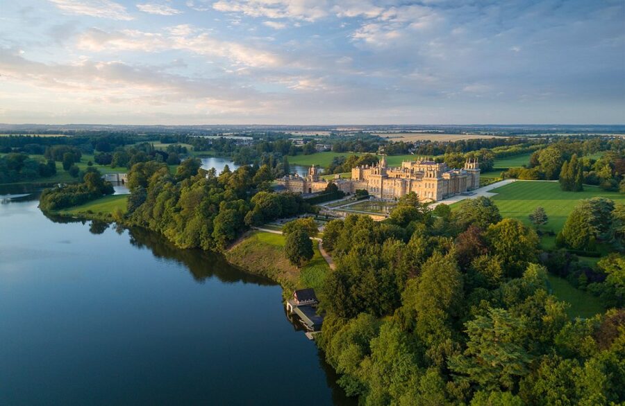 Aerial view of Blenheim Palace surrounded by a serene lake in England, showcasing its grandeur and natural beauty.
