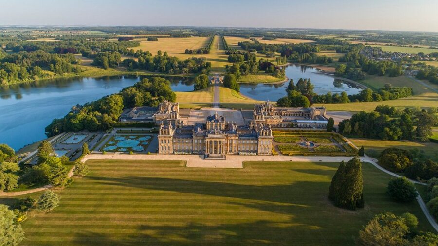 Aerial view of Blenheim Palace, a large mansion surrounded by lush trees in England.