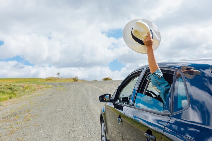 Car parked on scenic road with hand waving hat, symbolizing adventure and freedom.