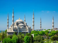The Blue Mosque in Istanbul, Turkey, showcases its stunning architecture on a sunny day, surrounded by vibrant greenery